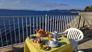 Taula preparada amb menjar per esmorzar a una terrassa amb vista al mar.