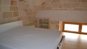 A bedroom with a large bed, stone walls, a wooden ceiling, and a skylight. - Le Terrazze B&B (Manduria)