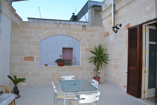A patio with a table and chairs, a potted plant, and a window with shutters.