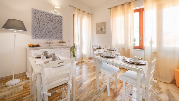 A dining area with white furniture, a table set for two, and a decorative wall piece. - Villa Iole (Carloforte)