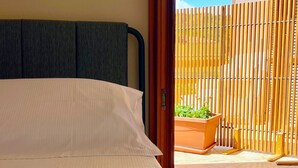 A bedroom with a bed, a wooden floor, and a view of a balcony with a wooden fence and a planter. - Villa Iole (Carloforte)