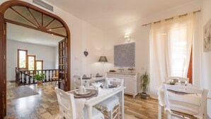 A dining area with a white table set for four, a potted plant, and a staircase leading to another room. - Villa Iole (Carloforte)