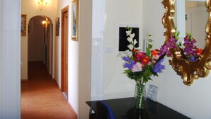 A hallway with a door leading to another room, a wall-mounted mirror, and a vase with flowers on a table. - Come D'Incanto a Napoli (Naples)