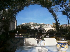 A table with a bowl and a plate, set against a backdrop of a cityscape with a hill and buildings. - Come D'Incanto a Napoli (Naples)