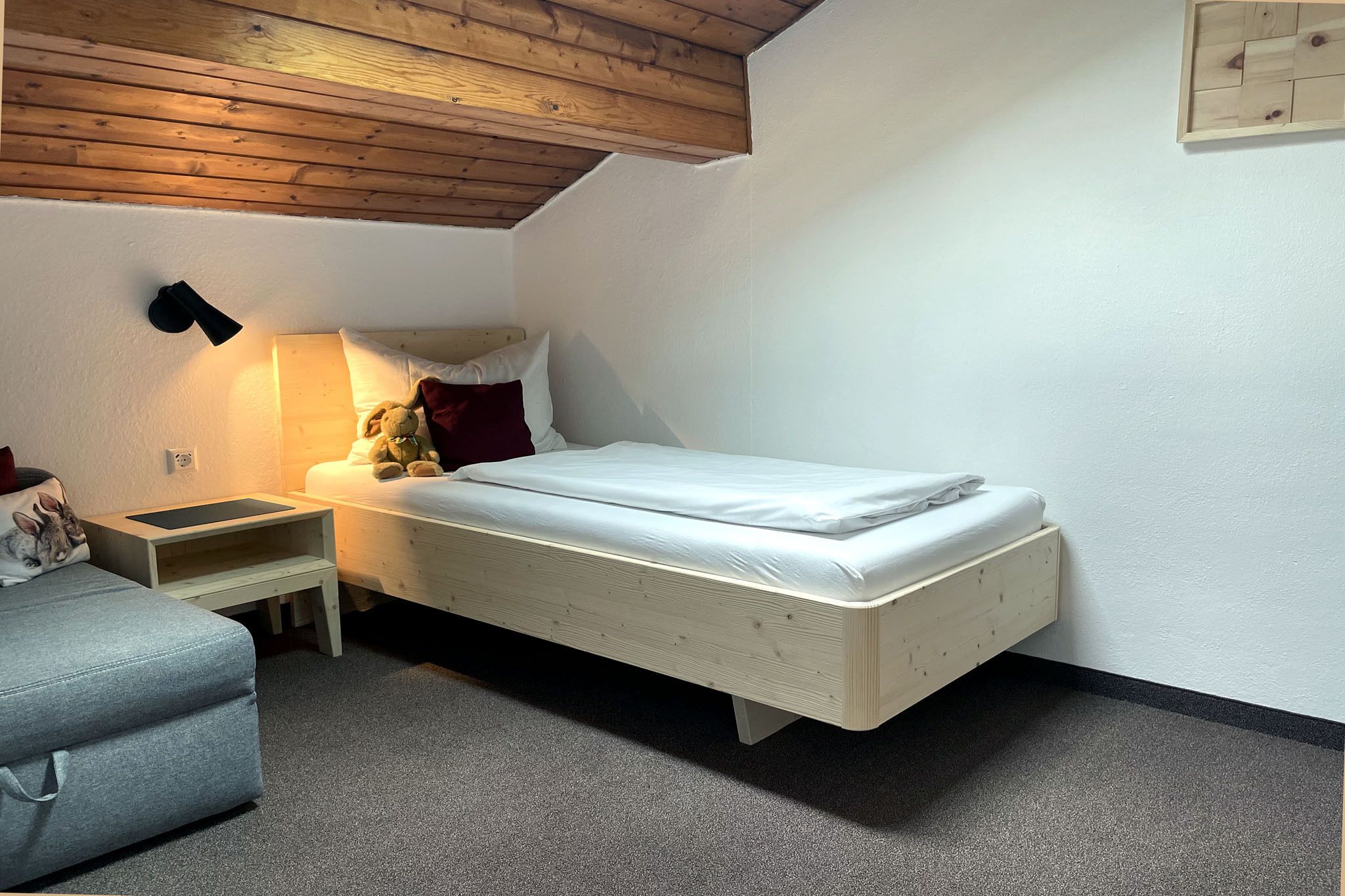 Un dormitorio pequeño y ordenado con una cama individual, una mesita de noche, una lámpara y una silla.