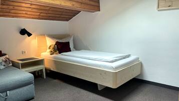 Un dormitorio pequeño y ordenado con una cama individual, una mesita de noche, una lámpara y una silla.