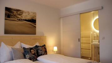 Une chambre d’hôtel avec un lit, des oreillers, un tableau accroché au mur, une lampe de chevet et une salle de bain visible à travers une porte ouverte.