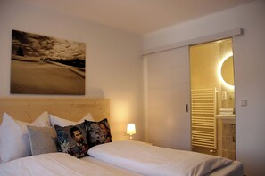 A hotel room with a bed, pillows, a wall-mounted painting, a bedside lamp, and a bathroom visible through an open door. - Pension Sonnenzeit (Reit im Winkl)