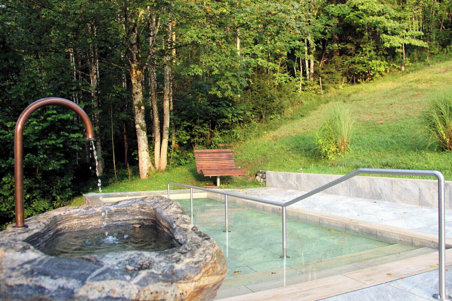 A hot spring area with a stone basin, a metal railing, and a wooden bench.
