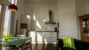 A compact kitchen with modern appliances, a dining area with a glass table, and a cozy seating area with a black sofa and green pillow. - Spitsbroek (Eede)