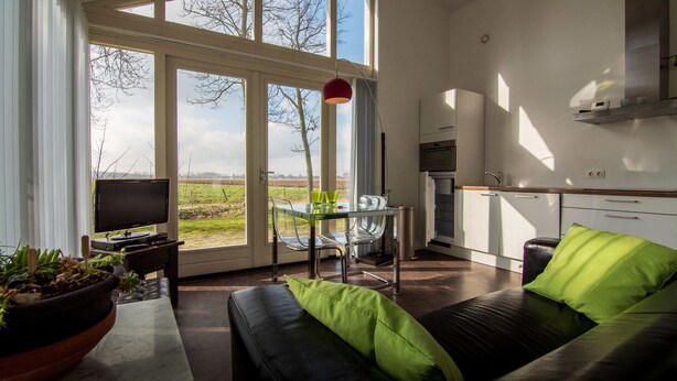 A modern kitchen with a dining area, a TV, and a sofa with green cushions. - Spitsbroek (Eede)