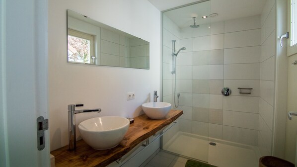 A modern bathroom with a wooden vanity, two white sinks, a large mirror, and a glass-enclosed shower area.