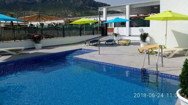 Ein Poolbereich mit freiem Blick auf die Berge im Hintergrund, umgeben von Liegestühlen und Sonnenschirmen.