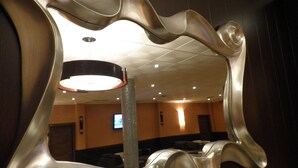 Ein Spiegel mit gewelltem Rahmen spiegelt einen Empfangsbereich mit einer gefliesten Säule, einem Fernseher und einer Tür wider.