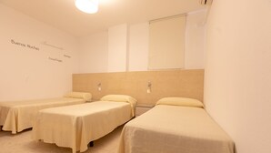 Habitació d'hotel amb tres llits individuals, cadascun amb frontal de fusta i una taula de nit.