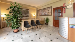 Rebedor d'hotel amb taulell de recepció, un quadre gran, un sofà i dues cadires.