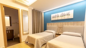 Una habitació d'hotel amb dos llits individuals, un bany i una obra d'art penjada a la paret.