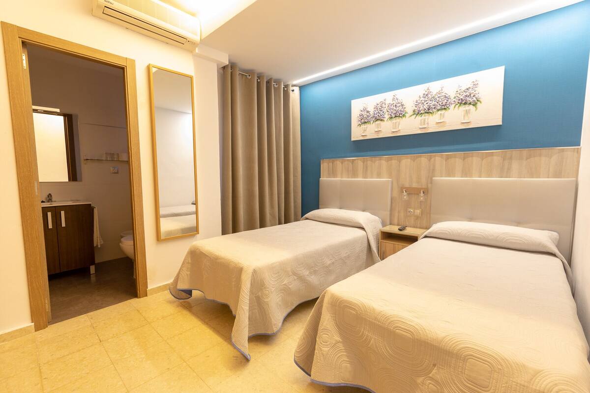 Una habitación de hotel con dos camas individuales, un baño y una obra de arte colgada en la pared.