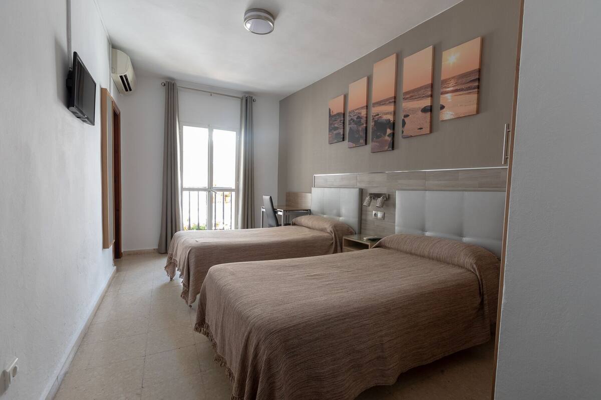 Habitación de hotel con dos camas, un ventanal grande, televisión de pantalla plana y obras de arte en la pared.