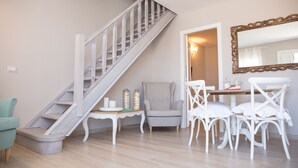 Una escalera con detalles de madera, un comedor con sillas blancas y una mesa, y un espejo grande en la pared.
