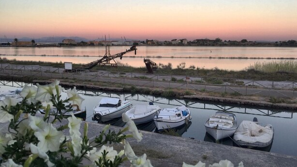 Un puerto deportivo con varias embarcaciones amarradas, una vía acuática y una costa distante con edificios.
