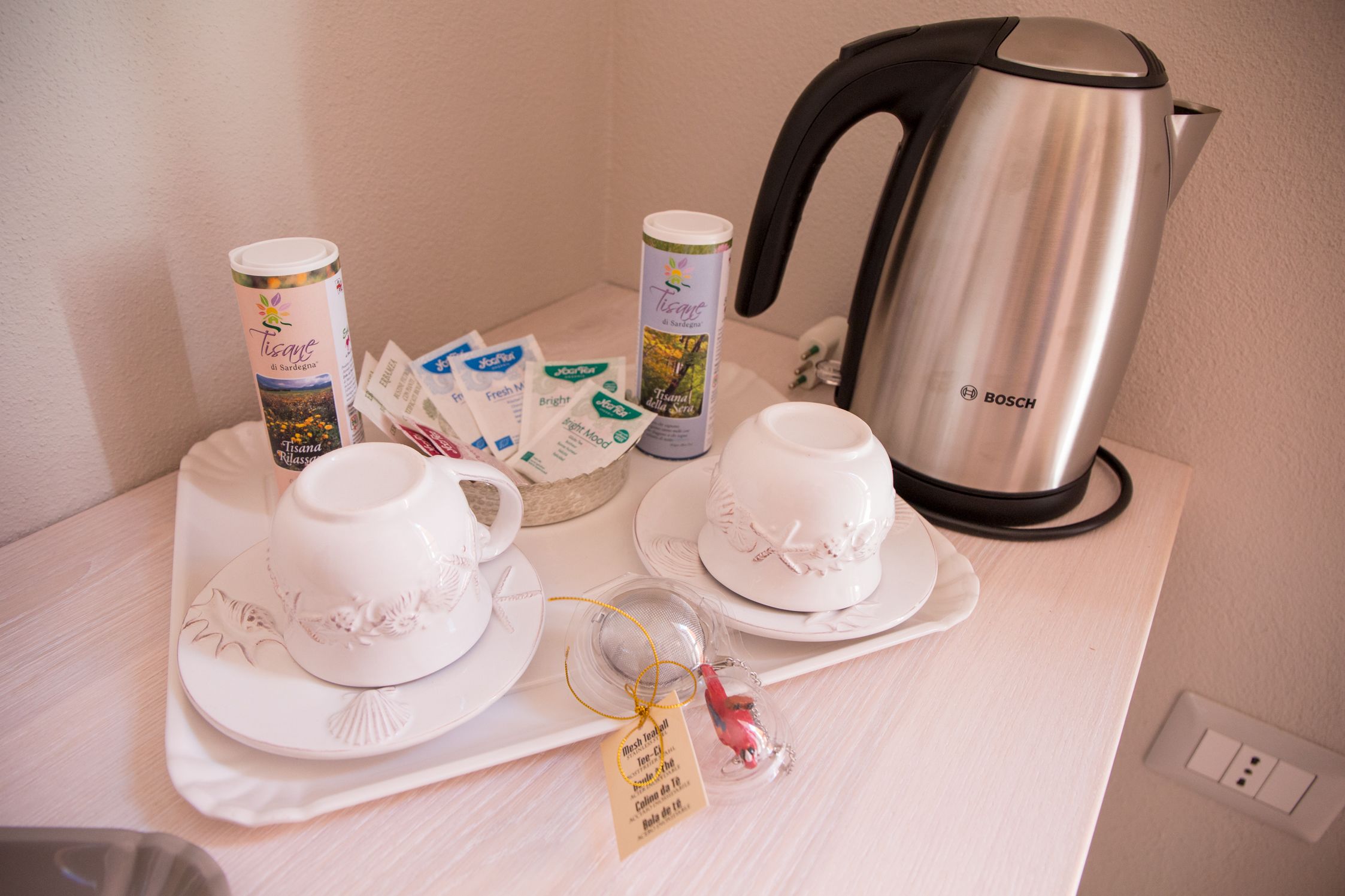 Une table de petit-déjeuner avec des tasses et des soucoupes à thé blanches, une machine à café et des sachets de thé, le tout disposé sur un plateau.