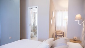 Un dormitorio con una cama grande, una silla, una mesita de noche y un baño visible a través de una puerta abierta.