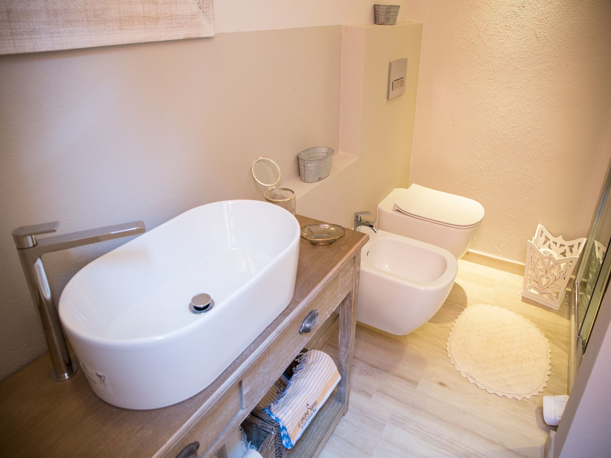 A bathroom with a white bathtub, a white toilet, and a bidet. There is a wooden vanity with a towel rack and a small trash bin.