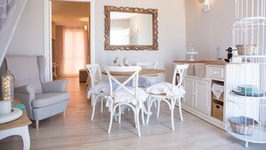 Un comedor con una mesa redonda y sillas blancas, un espejo sobre la mesa, y una escalera que lleva a otra habitación.