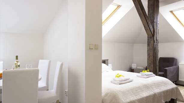 A modern, well-lit room with a high ceiling, a bed with white linens, a dining area with white chairs, and a large window providing natural light. - Residence Praha (Prague)