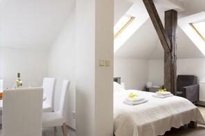 A modern, well-lit room with a high ceiling, a bed with white linens, a dining area with white chairs, and a large window providing natural light. - Residence Praha (Prague)