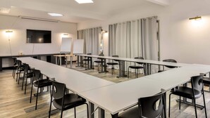 Een vergaderruimte met een lange tafel, zwarte stoelen, een whiteboard en een flatscreen-televisie.