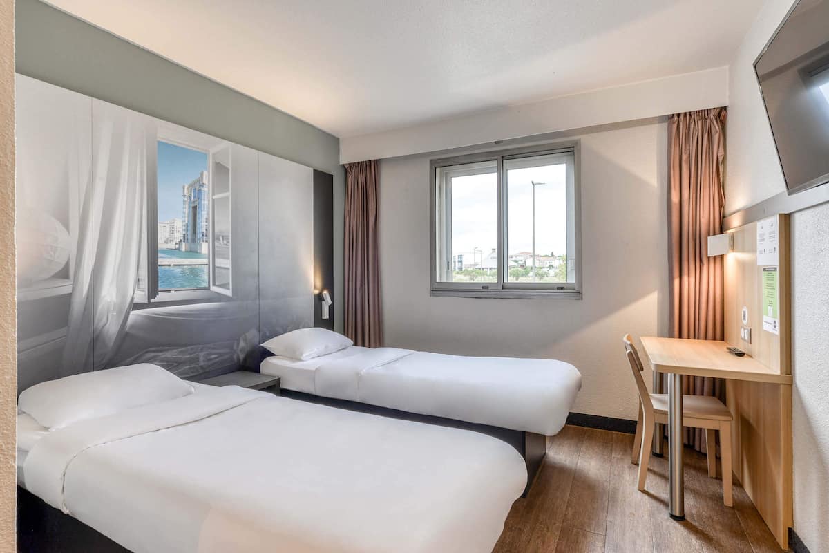 Een hotelkamer met twee bedden, een bureau en een raam met uitzicht op gebouwen en water.