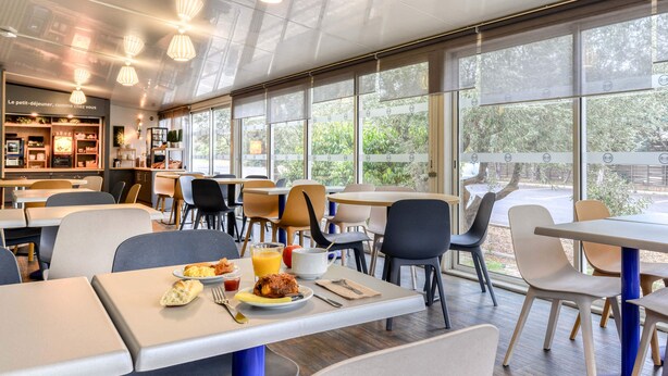 Een moderne eetruimte met tafels en stoelen, een ontbijtsetting en grote ramen met uitzicht op het omliggende landschap.