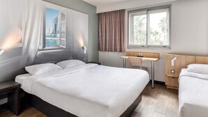 Een hotelkamer met een bed, een bureau, een stoel en een raam met uitzicht op gebouwen en palmbomen.