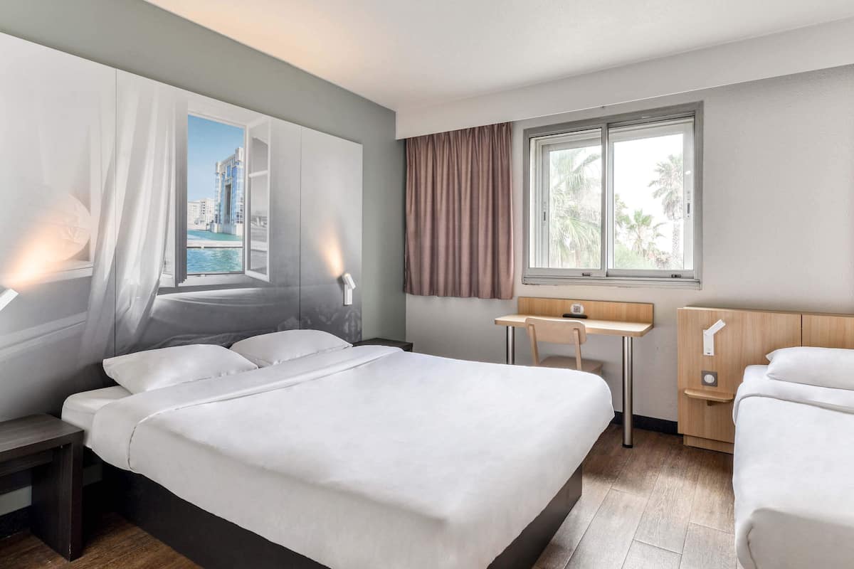Een moderne hotelkamer met een groot bed, een bureau en een raam met uitzicht op een stadsbeeld.