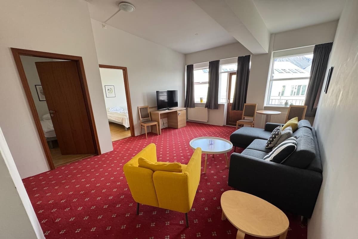 A modern living room with a red carpet, yellow and black sofas, a TV, and a small table.
