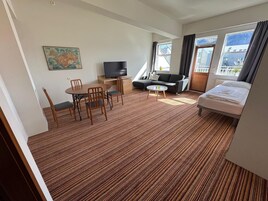 A hotel room with a bed, a sofa, a TV, a dining table with chairs, and a carpeted floor.