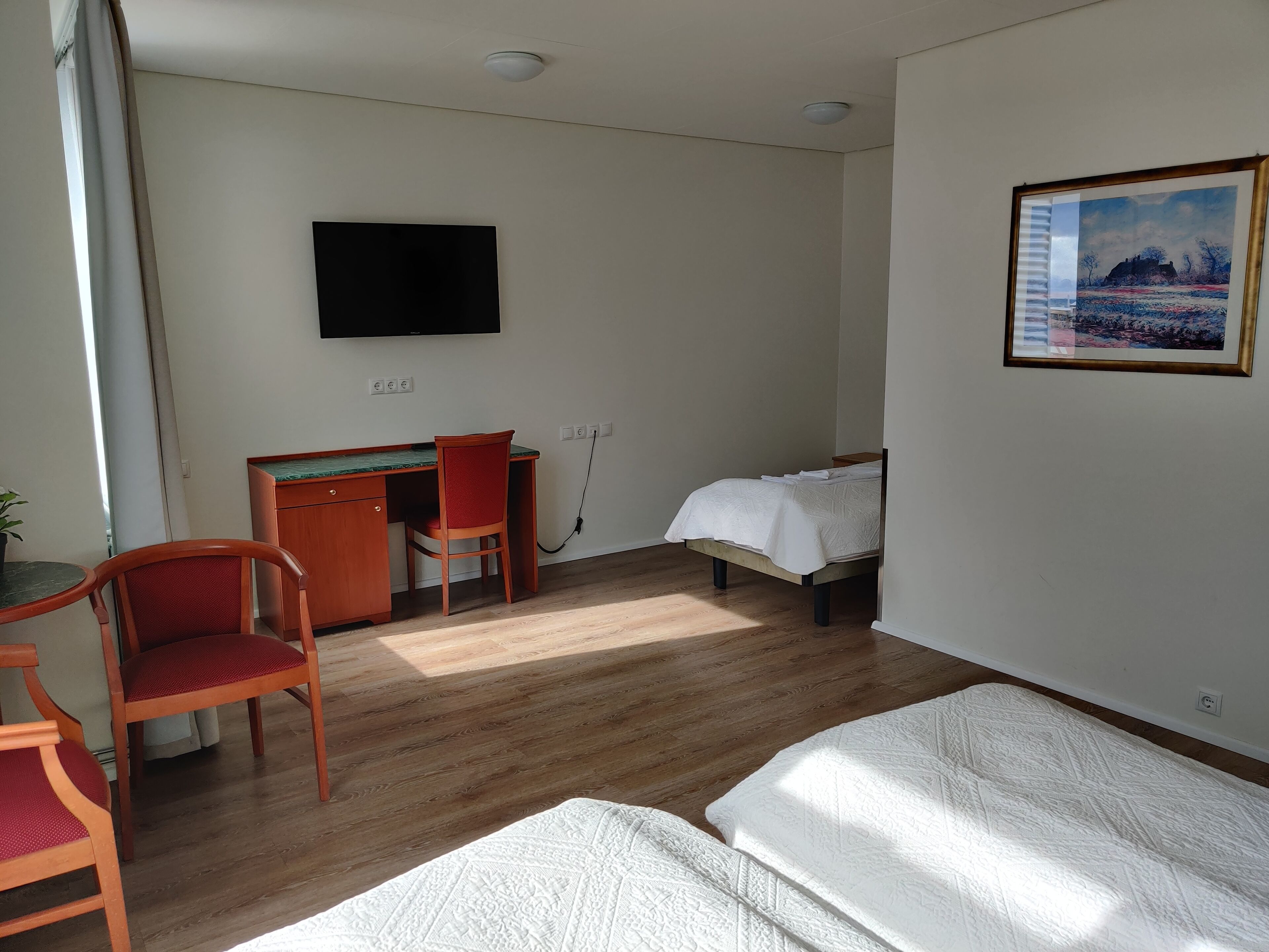 Habitación de hotel con escritorio, dos sillas, cama, televisor y un cuadro en la pared.