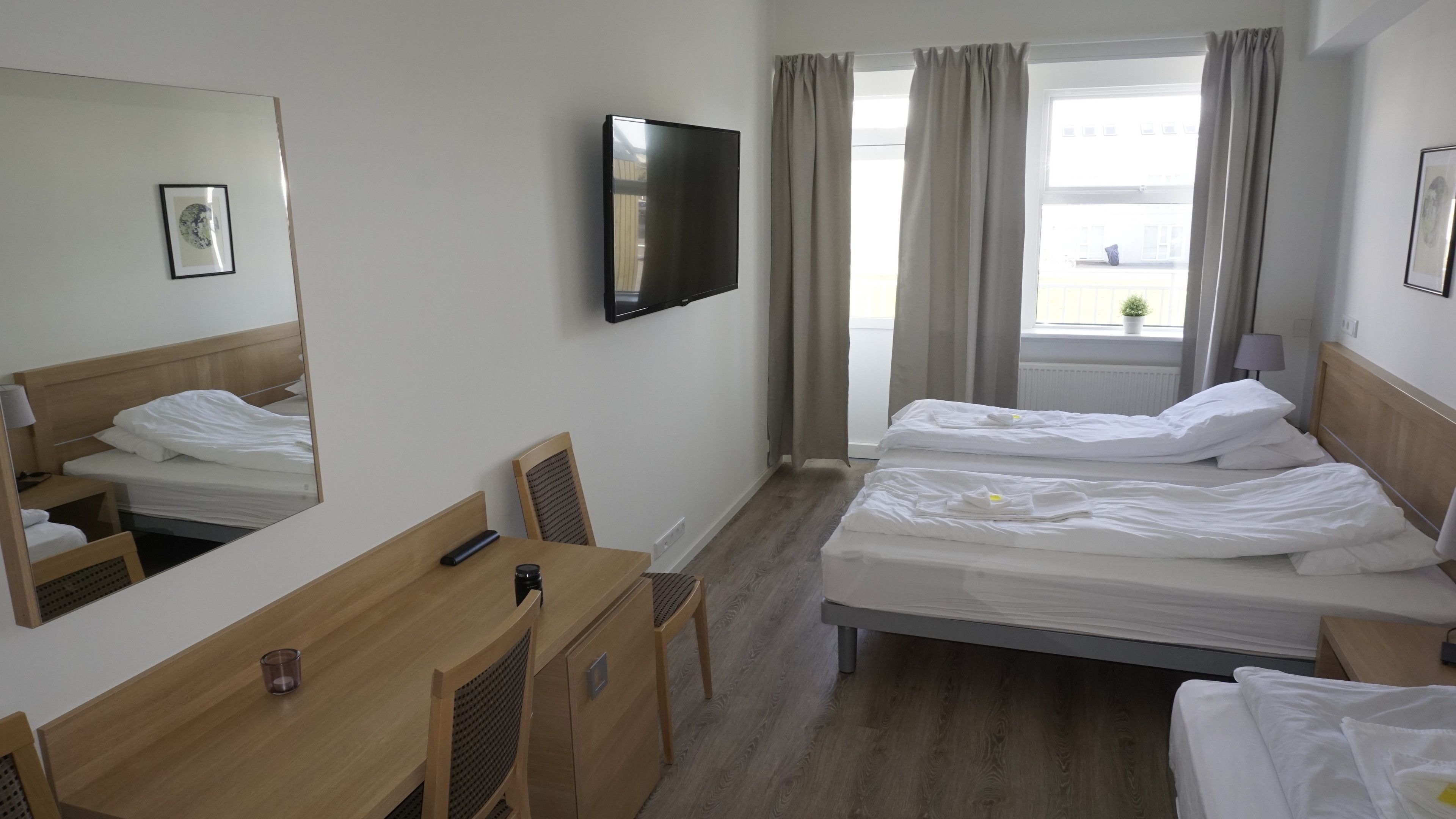 Une chambre d’hôtel avec deux lits, un bureau, une chaise, une télévision et une fenêtre avec des rideaux.