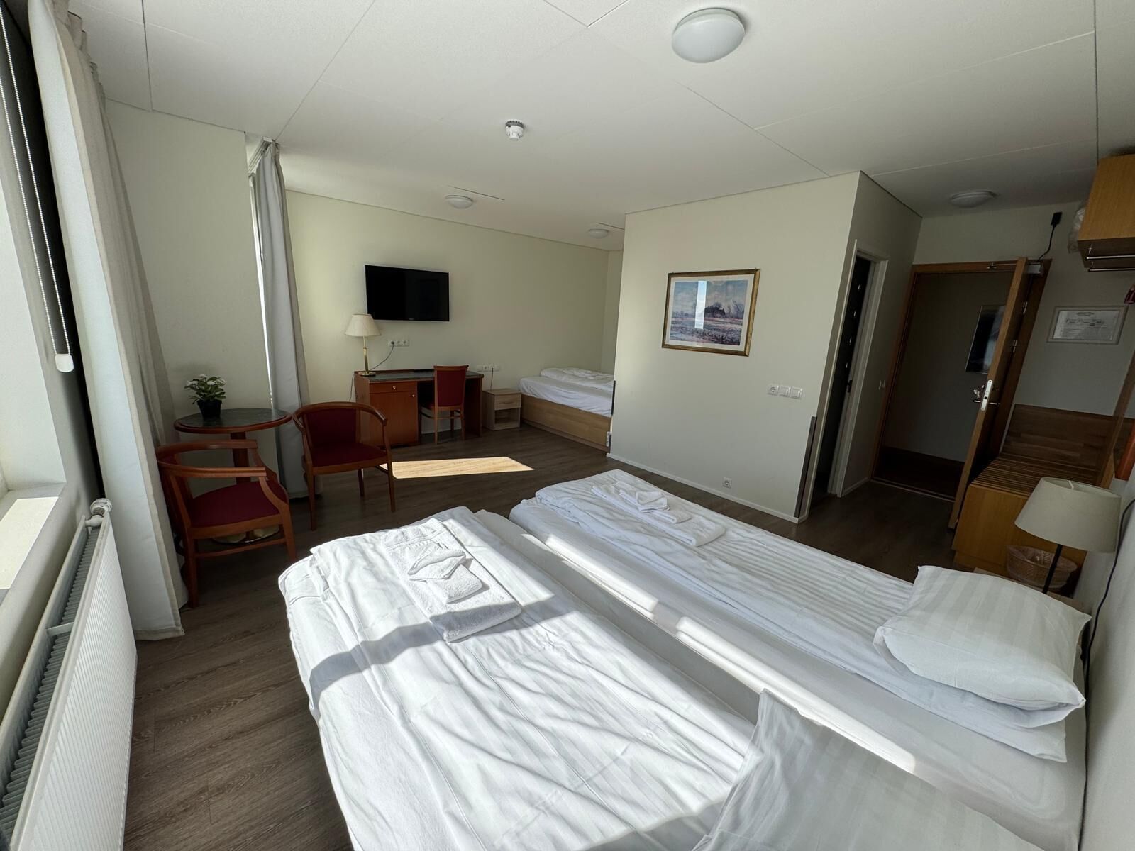 Habitación de hotel con dos camas, un escritorio, una silla, un televisor y un cuadro en la pared.