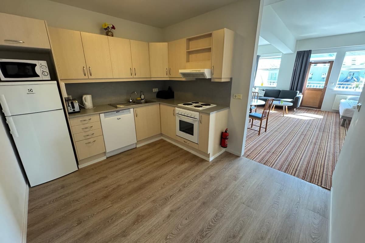 A modern kitchen with a microwave, dishwasher, stove, and sink. There is a dining area with a table and chairs visible through an open door.