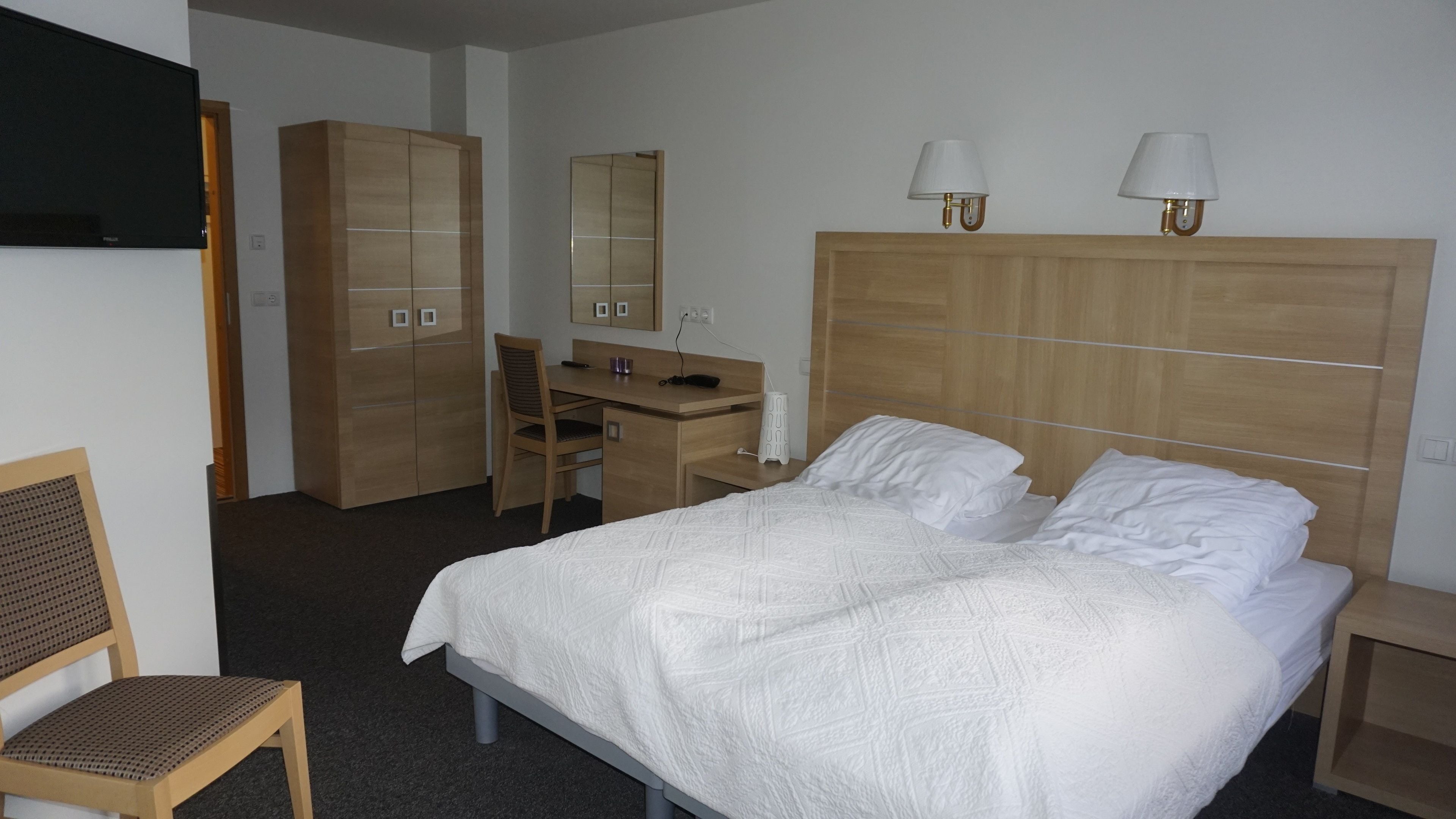 Una habitación de hotel con cama, escritorio, silla, armario y dos lámparas de noche.