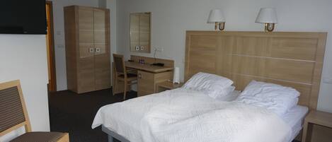 Una habitación de hotel con cama, escritorio, silla, armario y dos lámparas de noche.