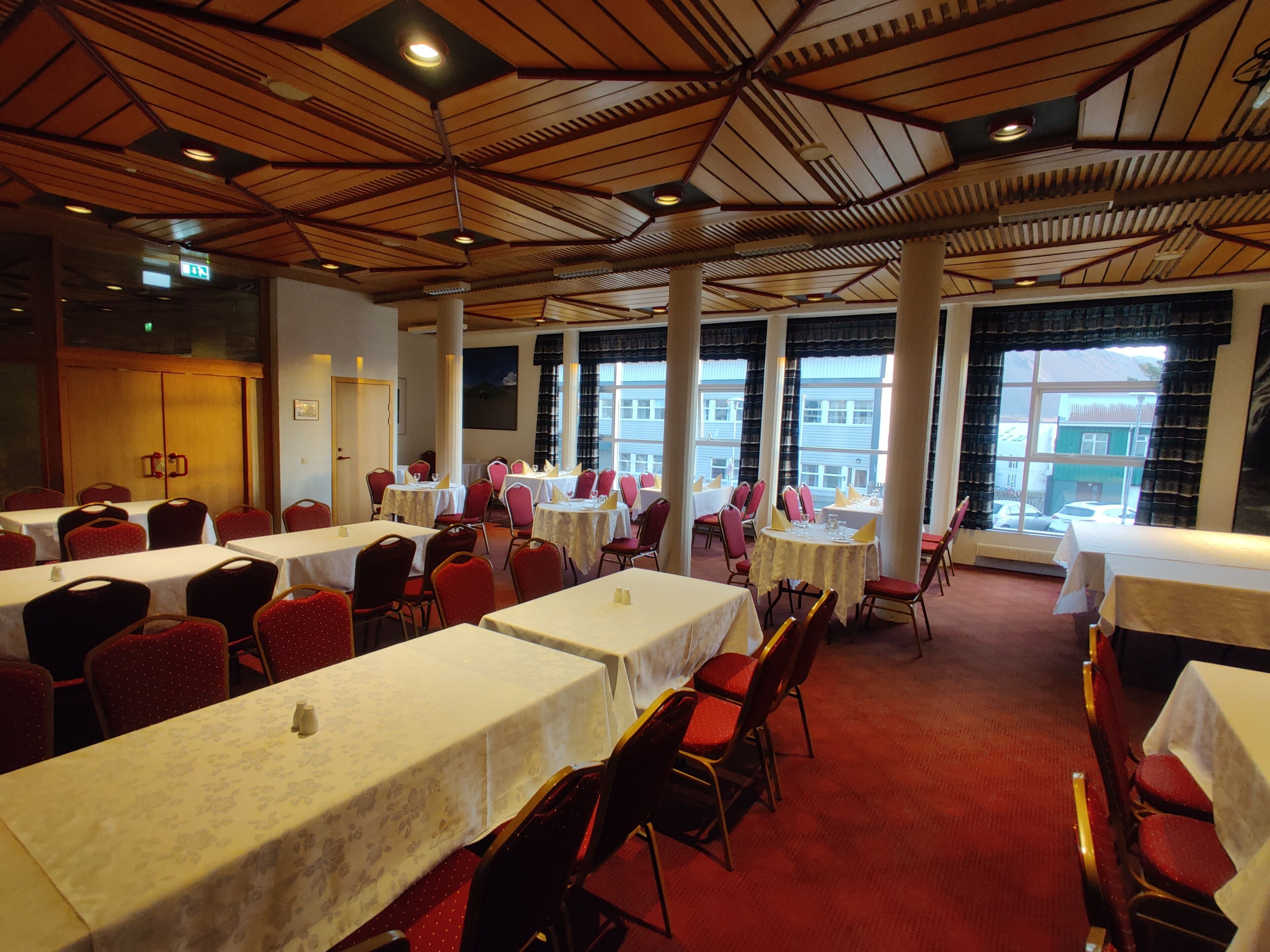 A dining area with multiple tables and chairs, large windows, and a high ceiling with wooden beams.