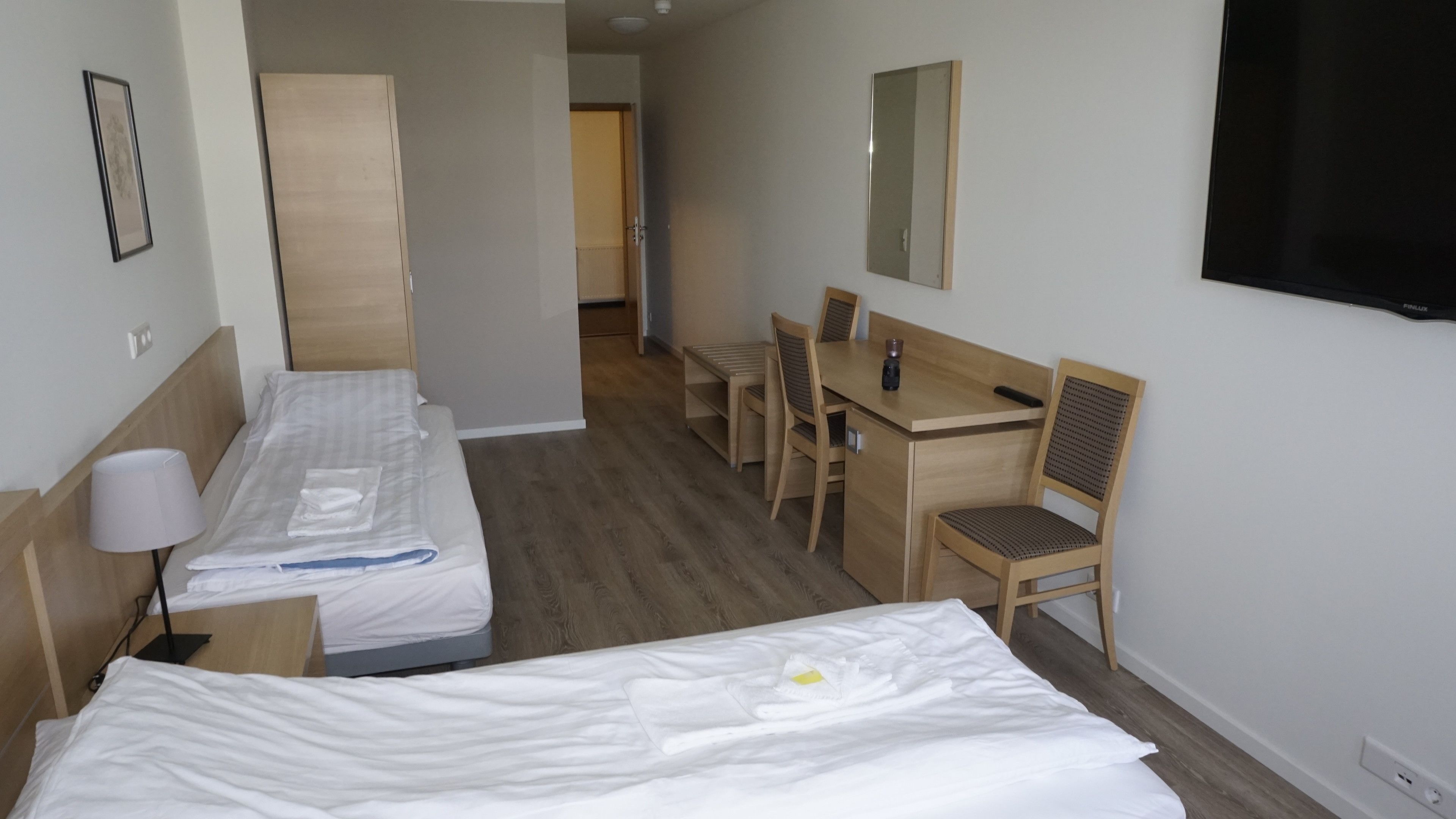 A hotel room with two single beds, a desk with a chair, a mirror, and a TV on the wall.