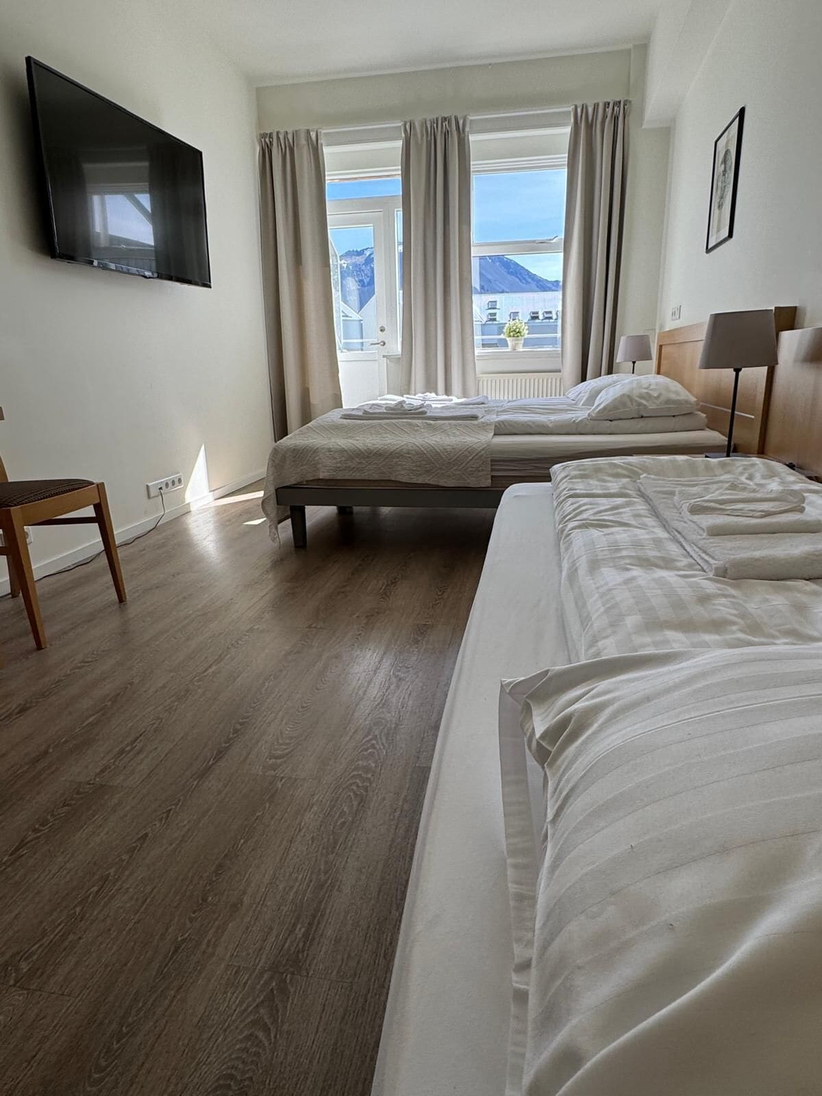 A hotel room with two beds, a TV mounted on the wall, a chair, and a window with curtains.