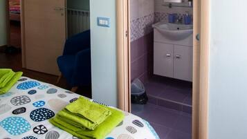 A bedroom with a bed, a chair, a door leading to a bathroom, and a ceiling light.