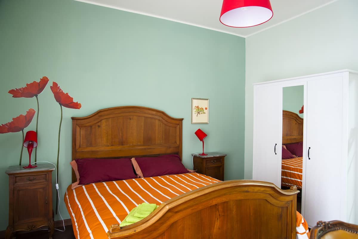 A bedroom with a wooden bed, two bedside tables, a nightstand, a mirror, and a wardrobe.