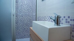 A bathroom with a white sink, a shower with purple mosaic tiles, and a wooden cabinet. - Alma B&B (Crotone)
